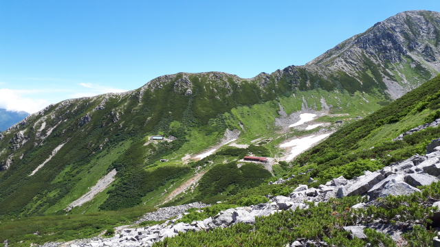 残雪が残る山肌と緑のコントラストが美しい、雄大な山岳風景です。
